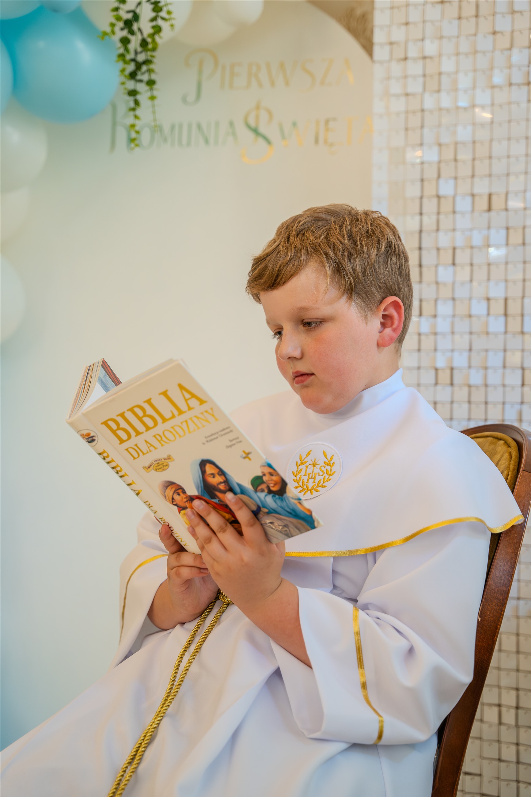 Dziecko w stroju komunijnym czytające Biblię podczas przyjęcia.