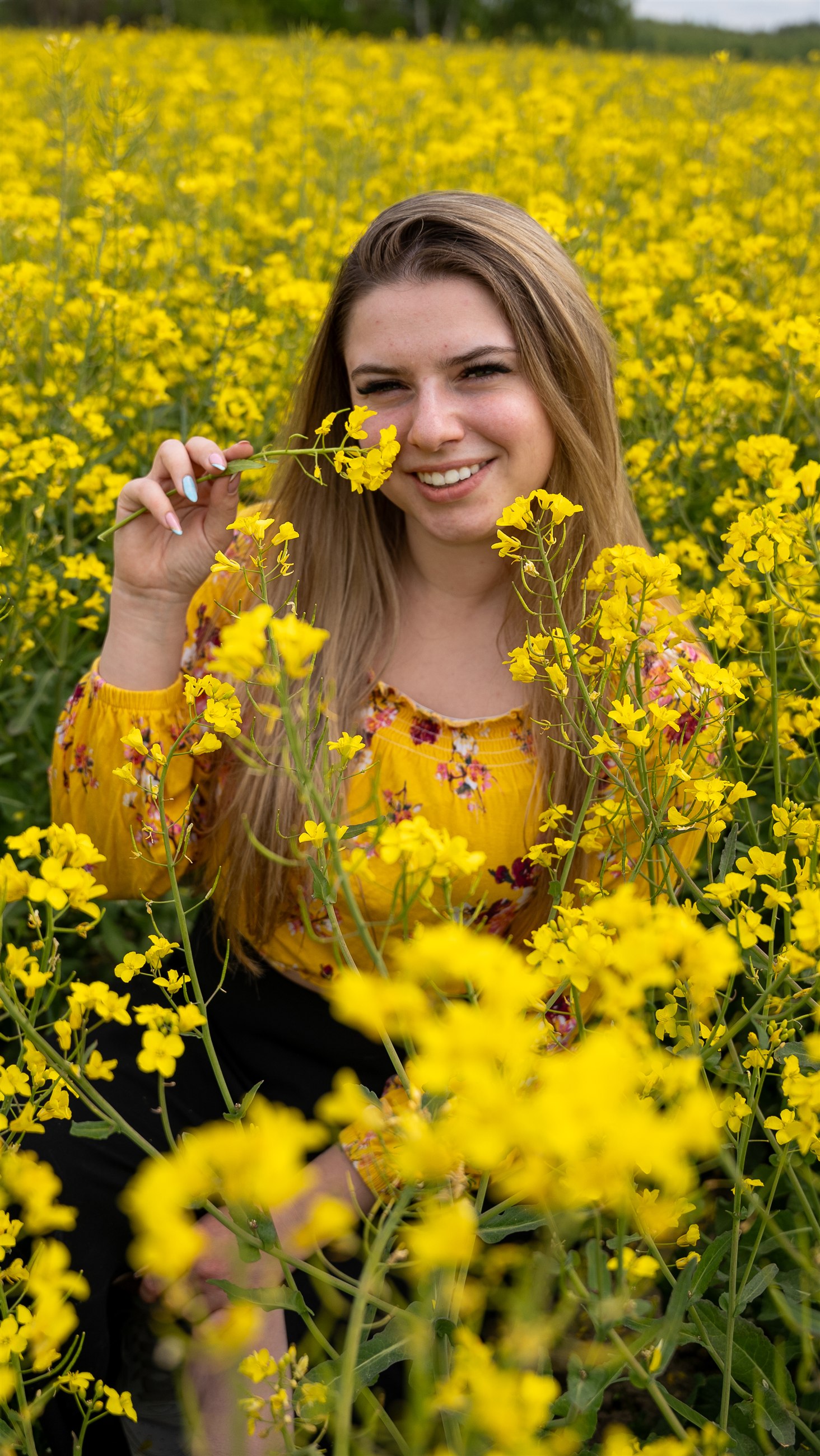 Uśmiechnięty portret kobiety wśród żółtych kwiatów rzepaku.